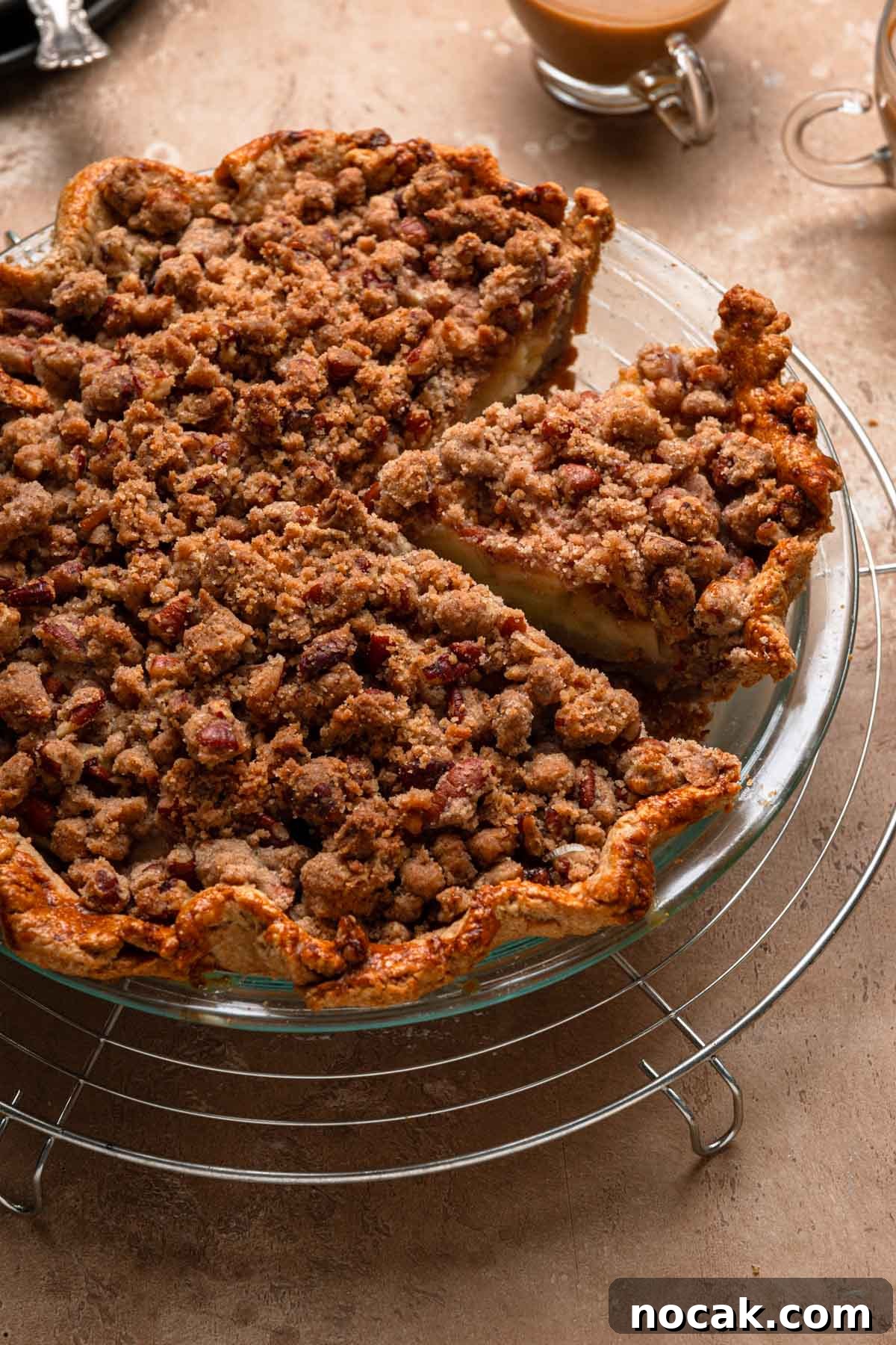 Sliced pear pecan pie with cups of coffee over a wire rack.