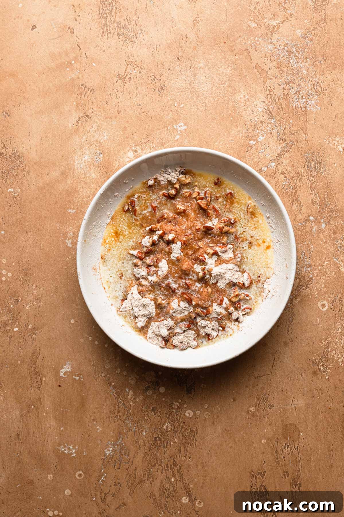 A bowl with flour, melted butter and chopped pecans.