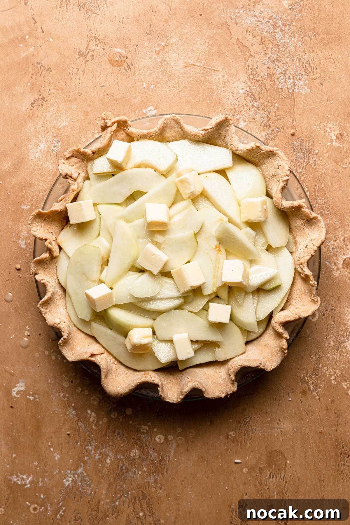 Layered pears in pie dish dotted with butter.