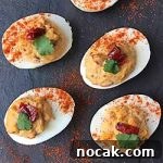 Square top-down view of chipotle deviled eggs, garnished with fresh herbs and a piece of red pepper, and sprinkled with paprika.