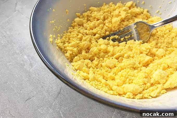 Chipotle Deviled Eggs with Smoky-Spicy Kick 7 Horizontal image of mashing yolks in a bowl with a metal fork