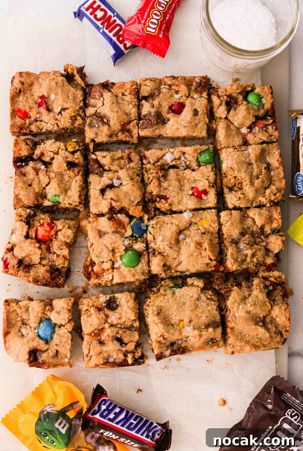 Leftover Halloween Candy Cookie Bars Recipe for Using Candy Up 2 Leftover Halloween candy cookie bars sliced on parchment paper with mini candy bars scattered around them.