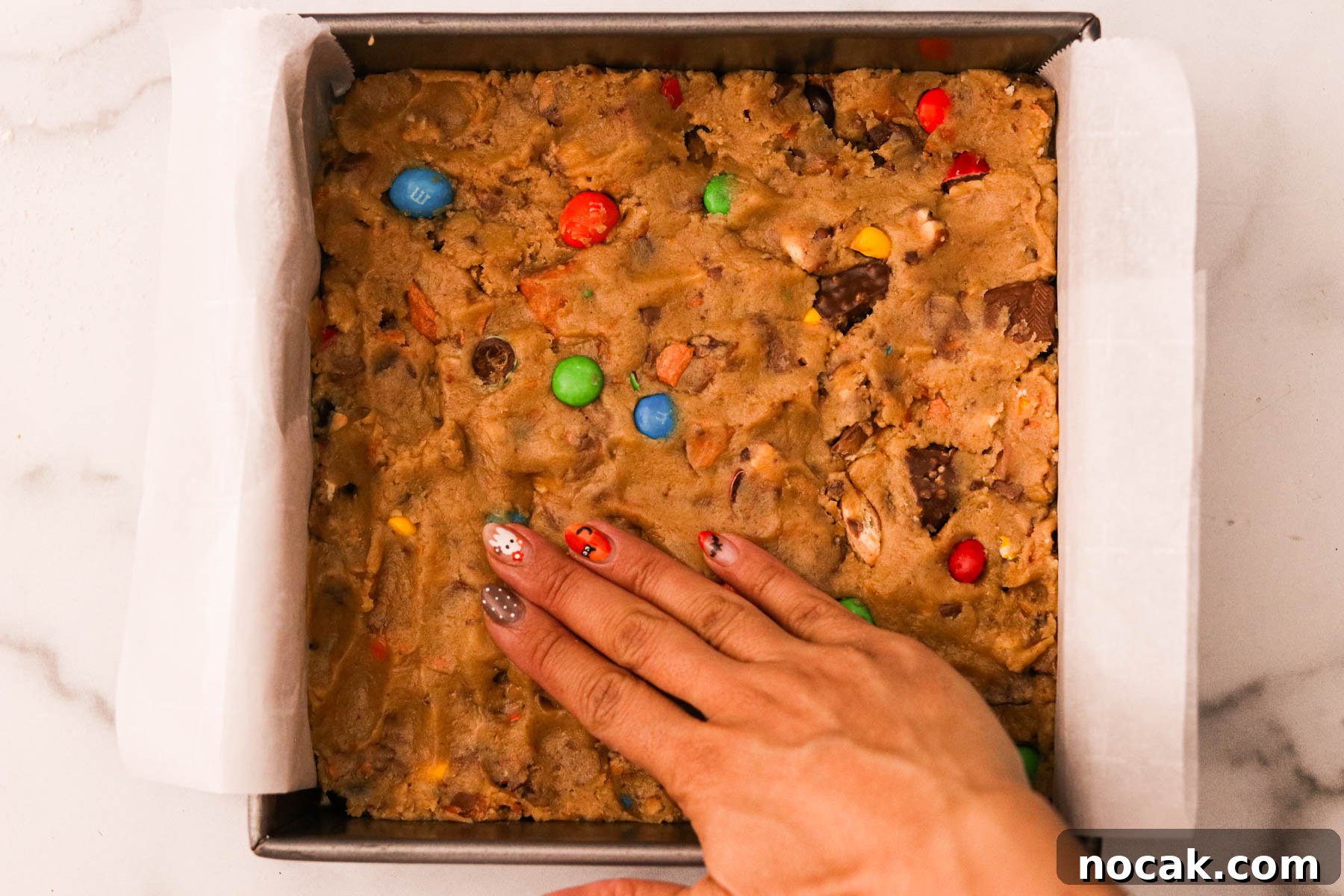 Leftover Halloween Candy Cookie Bars Recipe for Using Candy Up 8 A hand pressing dough mixture evenly into a parchment lined pan.