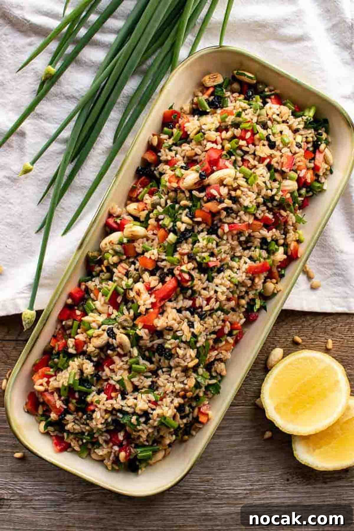 Hearty Brown Rice Salad with Fresh Veggies and Lemon Vinaigrette 2 Brown rice salad in oblong plate with spring onions and lemon.