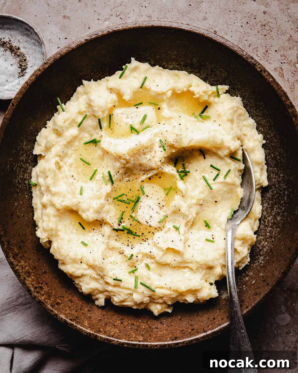 Creamy Horseradish Mashed Potatoes Recipe for Flavorful Sides 2 A rustic bowl filled with creamy horseradish mashed potatoes topped with melted butter, chopped chives, and black pepper, with a spoon resting in the bowl.