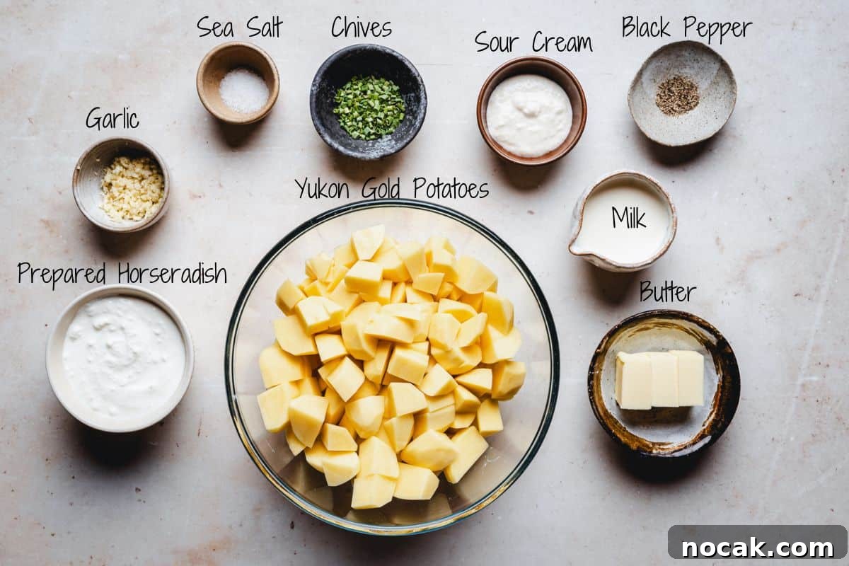 Creamy Horseradish Mashed Potatoes Recipe for Flavorful Sides 3 A bowl of cubed Yukon Gold potatoes surrounded by small bowls of sea salt, chives, sour cream, black pepper, minced garlic, prepared horseradish, milk, and butter on a light surface.