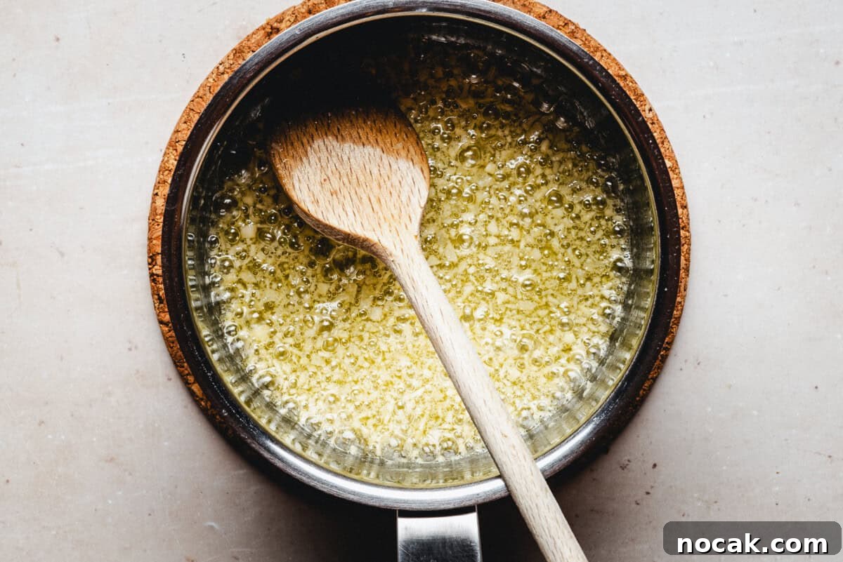 Creamy Horseradish Mashed Potatoes Recipe for Flavorful Sides 5 A wooden spoon rests in a saucepan filled with bubbling melted butter on a light-colored surface.