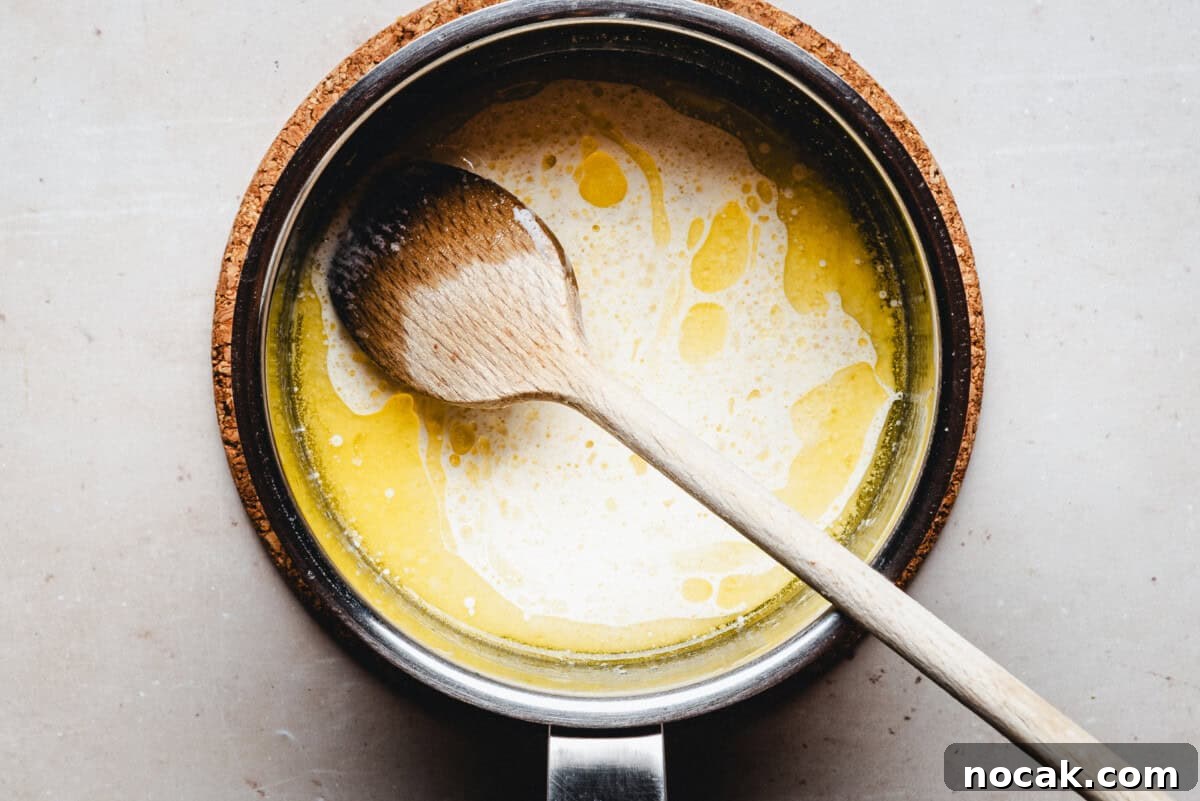 Creamy Horseradish Mashed Potatoes Recipe for Flavorful Sides 6 A wooden spoon rests in a saucepan filled with melted butter and cream, sitting on a cork trivet atop a light-colored surface.
