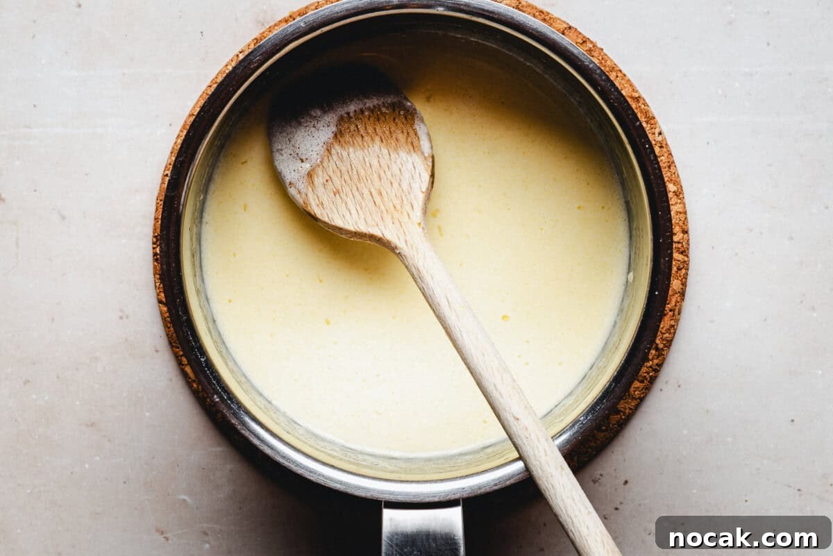 Creamy Horseradish Mashed Potatoes Recipe for Flavorful Sides 7 A saucepan filled with a creamy yellow sauce, with a wooden spoon resting inside, seen from above on a light-colored surface.