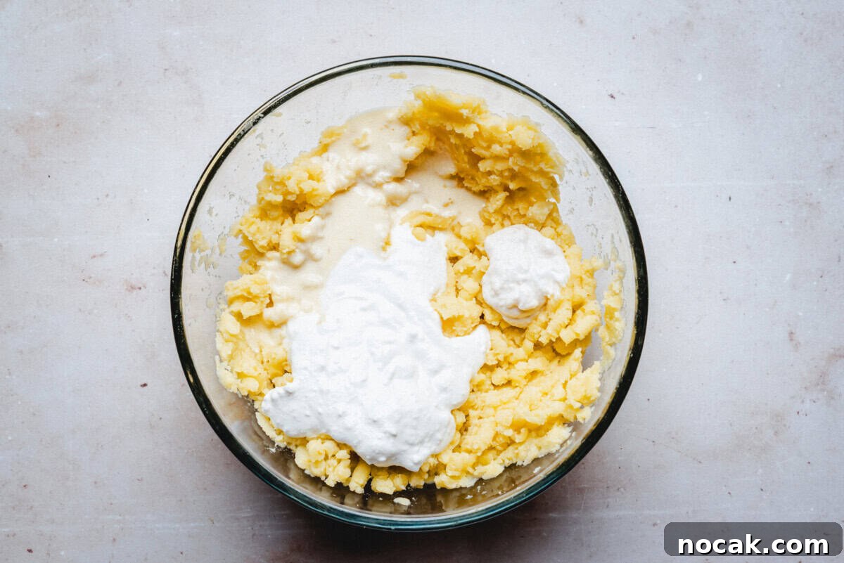 Creamy Horseradish Mashed Potatoes Recipe for Flavorful Sides 9 A glass bowl filled with mashed potatoes topped with a dollop of sour cream, sitting on a light-colored surface.