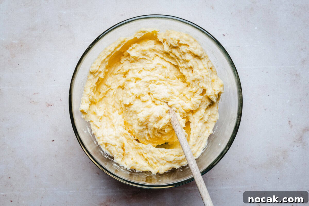Creamy Horseradish Mashed Potatoes Recipe for Flavorful Sides 10 A glass bowl filled with a creamy, yellow mashed potatoes being mixed with a wooden spoon, placed on a light-colored countertop.
