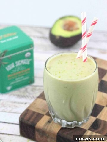 Banana matcha smoothie in a glass with red straws on a checkered wooden currant board.