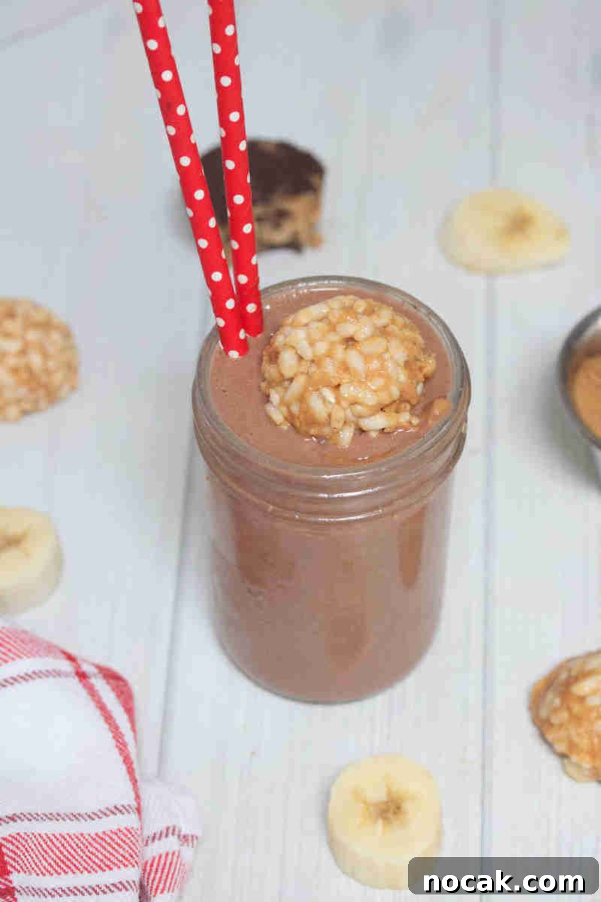 Peanut Butter Cup Protein Shake — 22g Protein Per Serving 8 Chocolate peanut butter cup smoothie in mason jar topped with peanut butter bomb in it and red straws in it.