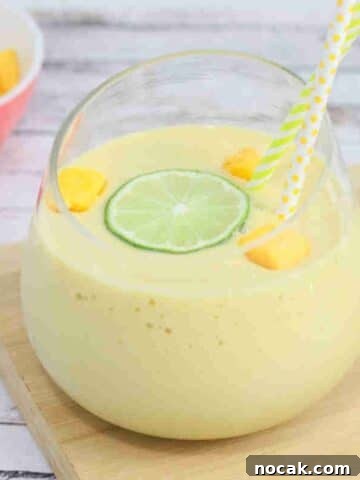 Mango protein smoothie in a glass on a cutting board topped with lime and mango.