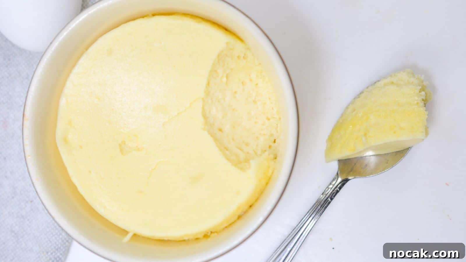 30 Christmas Desserts That Steal the Spotlight from Cookies 6 A ramekin of creamy, smooth cheesecake with a spoon resting beside it, taking out a scoop on a white background.
