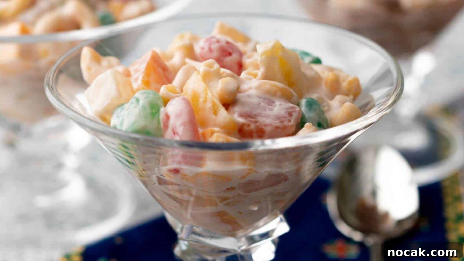 30 Christmas Desserts That Steal the Spotlight from Cookies 10 A glass bowl filled with a creamy fruit salad, featuring colorful fruits and marshmallows, placed on a blue cloth.