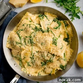 A frying pan filled with ravioli in a creamy lemon sauce, topped with grated cheese and rocket, with lemon wedges and herbs on the side.