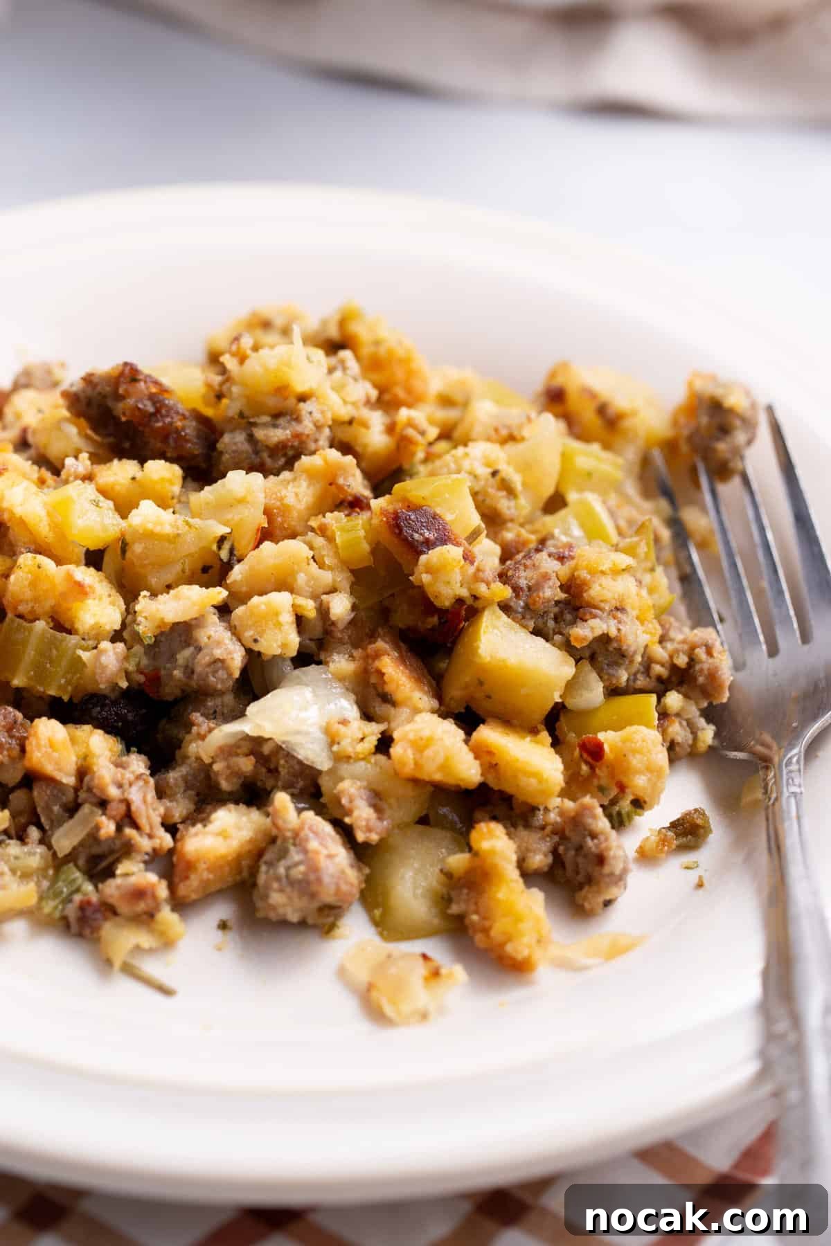 Sausage and Apple Stuffing Recipe for Holiday Feasts 7 Close up image of a serving of sausage and apple stuffing served on a white round plate with a silver fork.