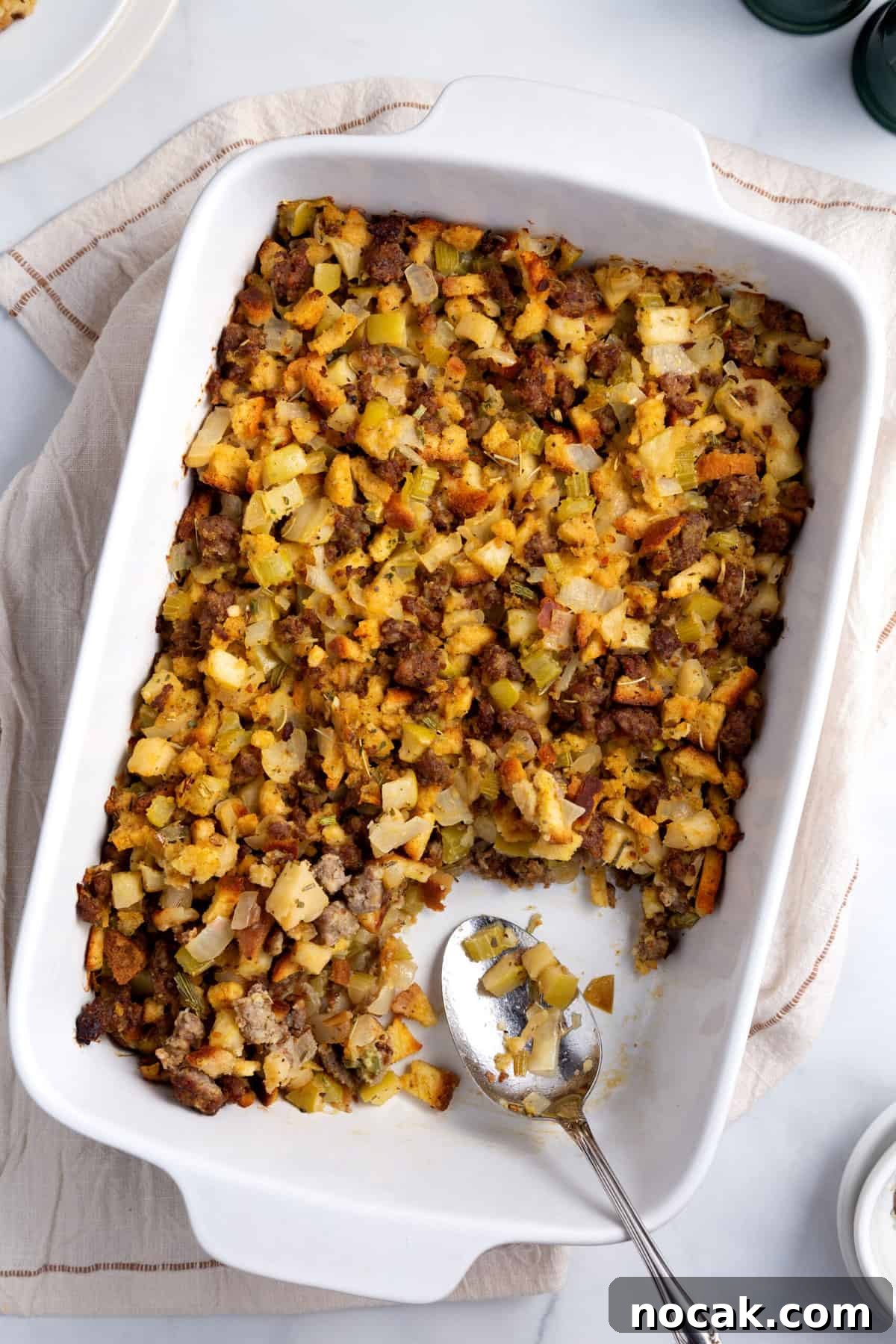 Sausage and Apple Stuffing Recipe for Holiday Feasts 3 Top down image of sausage and apple stuffing baked in a white casserole dish with metal serving spoon.