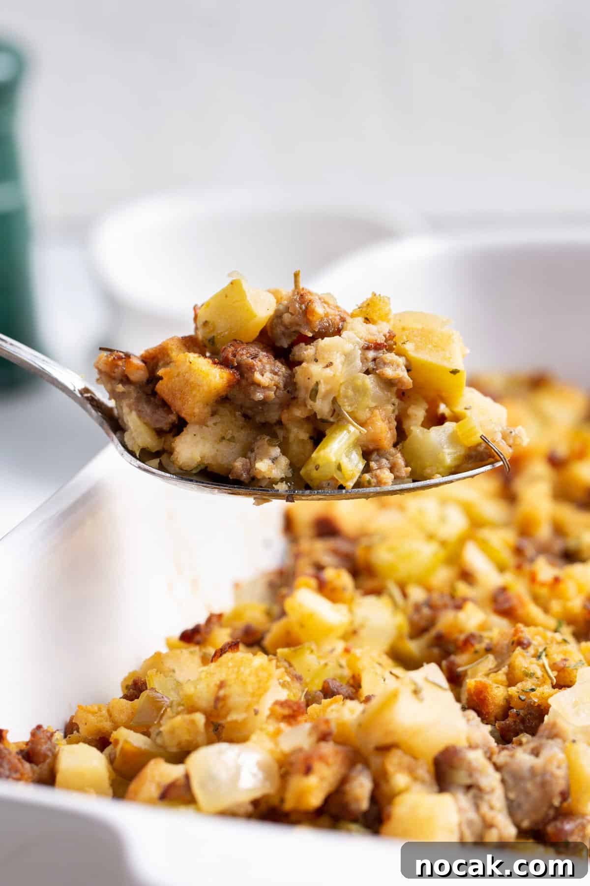 Sausage and Apple Stuffing Recipe for Holiday Feasts 6 Close up of a spoonful of sausage and apple stuffing, rest of sausage and apple stuffing in a white casserole dish in the background.