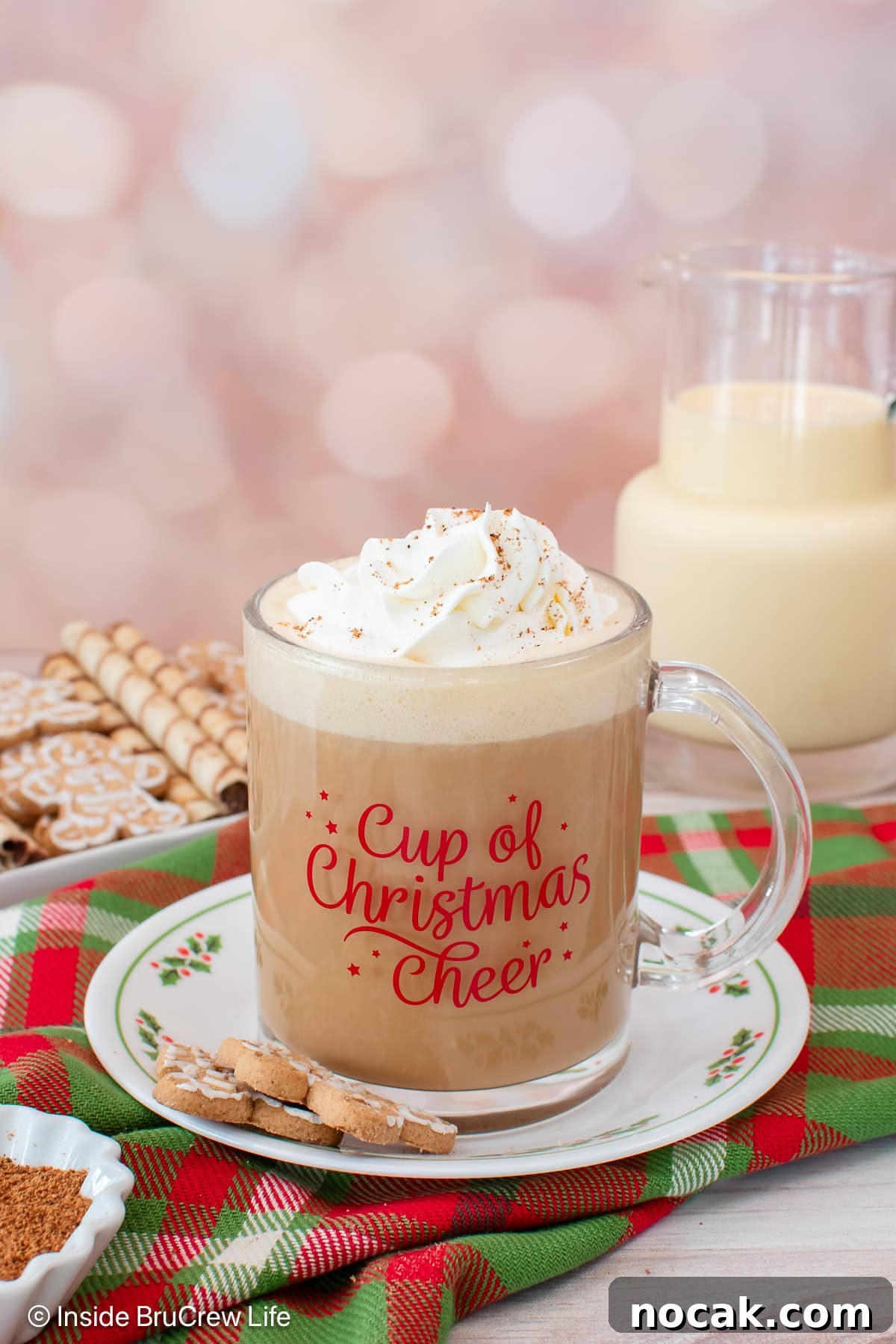 An eggnog latte topped with a swirl of whipped cream in a festive mug, set on top of a red and green plaid cloth.
