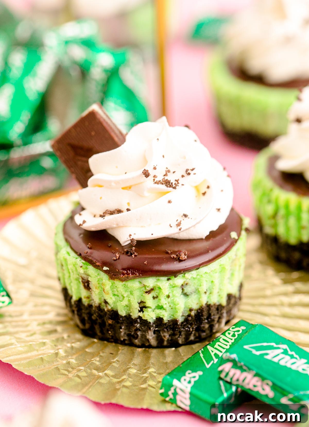Oreo Chocolate Mint Mini Cheesecakes for St. Patrick’s Day 2 Close up photo of a mini chocolate mint cheesecake on a gold foil cupcake liner on a pink surface.