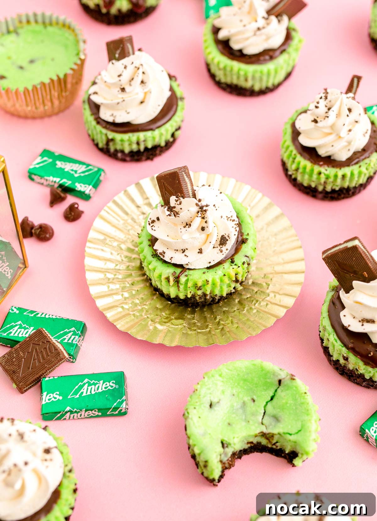 Oreo Chocolate Mint Mini Cheesecakes for St. Patrick’s Day 3 Mini mint oreo chocolate cheesecakes on a pink surface with andes mint candies around them.