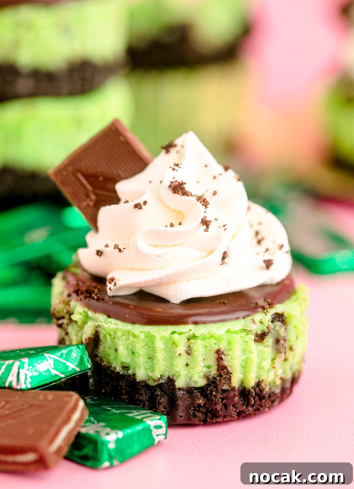 Oreo Chocolate Mint Mini Cheesecakes for St. Patrick’s Day 6 Mini Oreo Mint cheesecakes on a pink surface with mint candies around them.