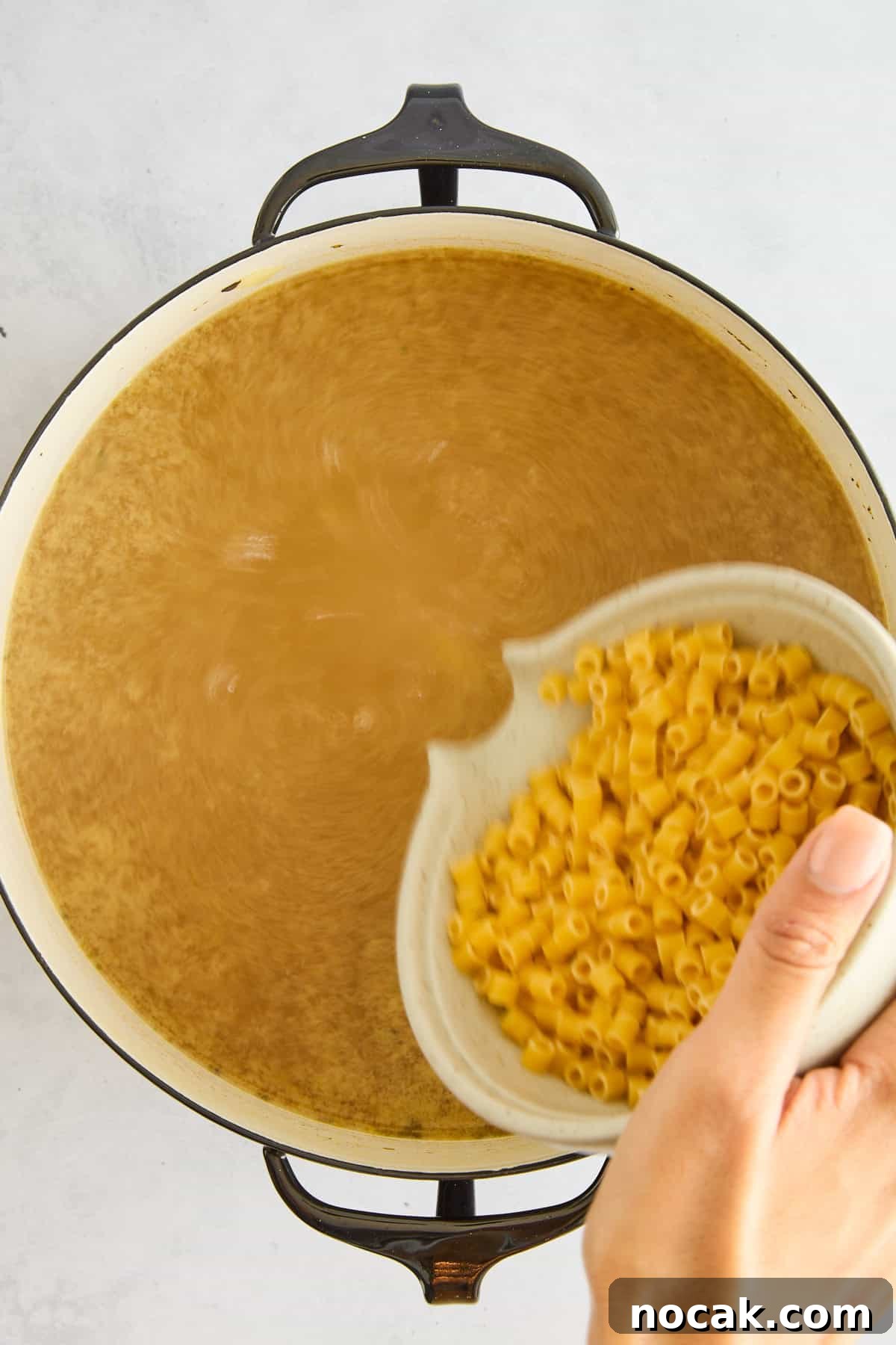Chicken Noodle Soup with Ditalini: Homemade Comfort Recipe 7 Raw ditalini pasta being poured into a pot of chicken noodle soup.