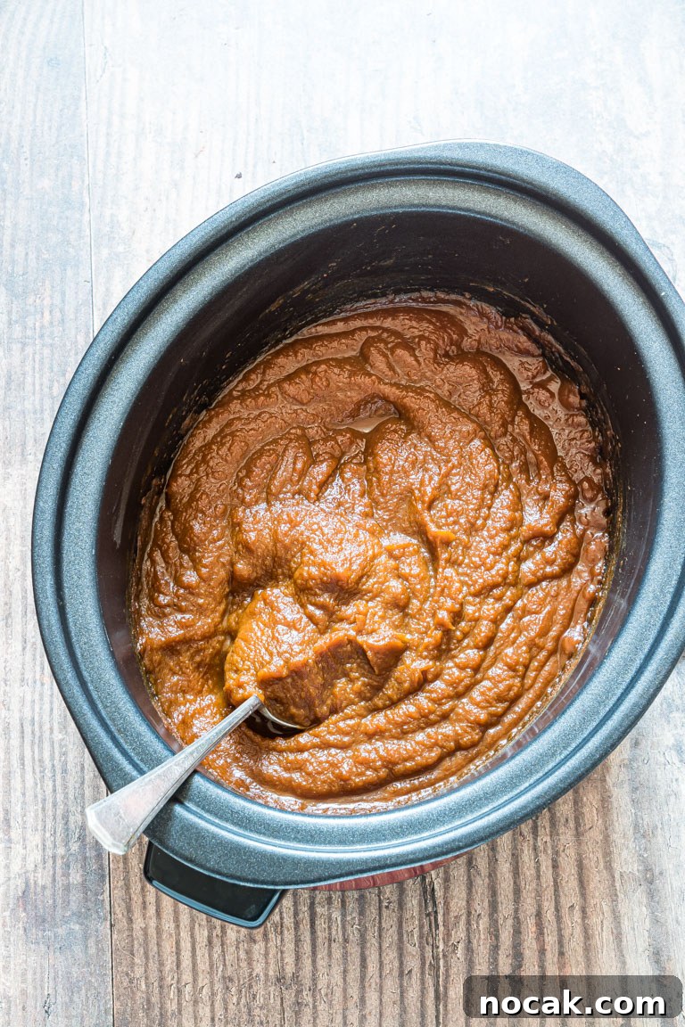 Slow-Cooker Pumpkin Butter Recipe for Fall Spreads and Gifts 2 Creamy pumpkin butter in a slow cooker with a spoon