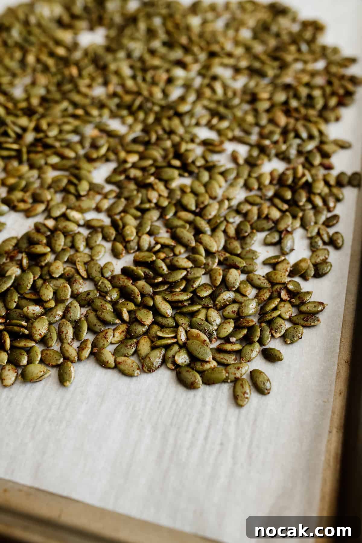 Pepitas Explained: What They Are and How to Use Them 3 seasoned raw pepitas on a parchment lined baking sheet prior to roasting in the oven.