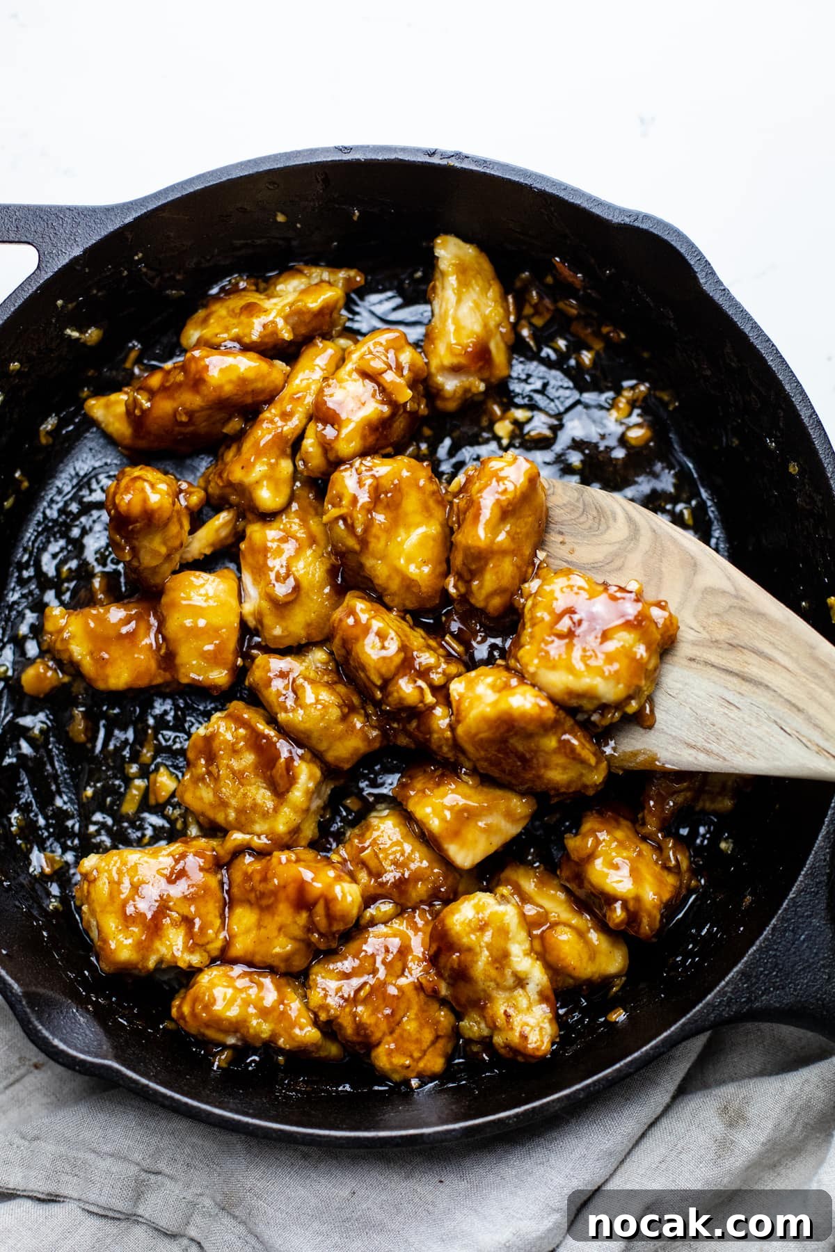 A black cast iron pan with honey sesame chicken in it with a wooden spoon.