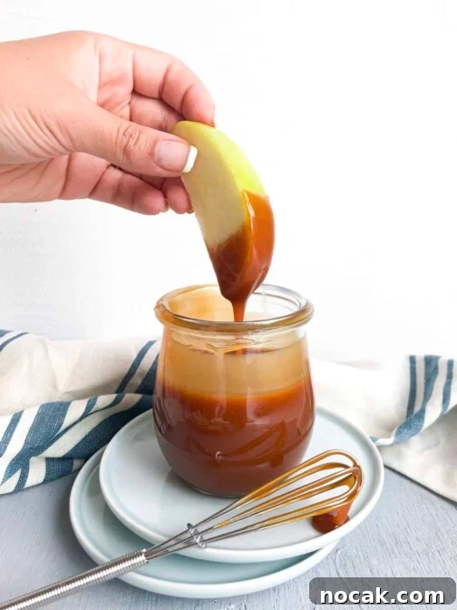 A green apple dipping into a jar of caramel