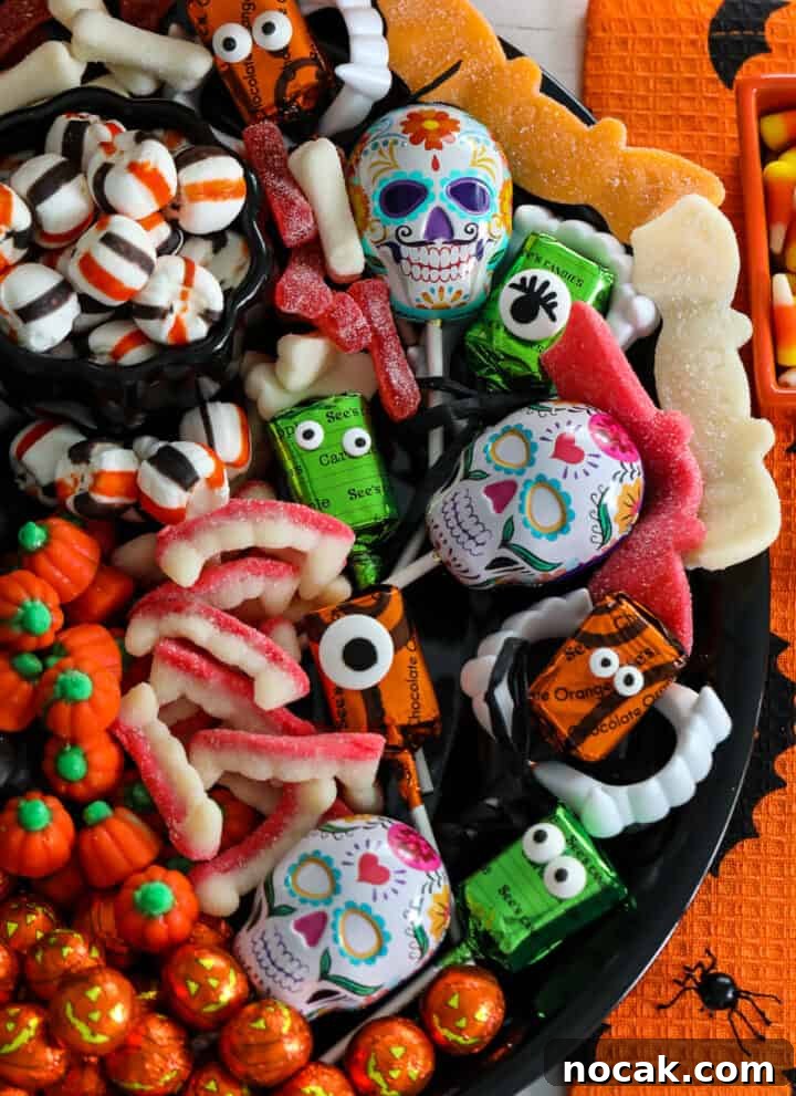 A Halloween candy board on a black tray loaded with candy pumpkins and gummy candy.