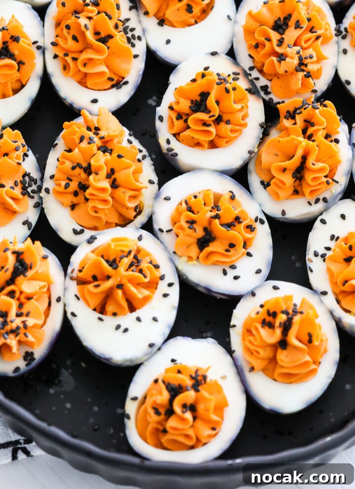 A black platter filled with Halloween deviled eggs sprinkled with black sesame seeds.
