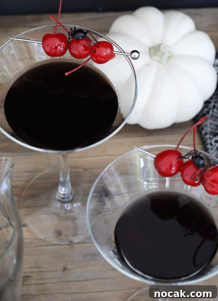 Two Halloween black drinks garnished with cherries and a small spider.