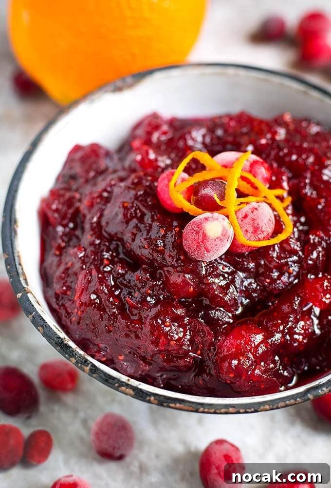 Thanksgiving Recipes for Instant Pot: Fast Holiday Favorites 22 Cranberry Sauce in a white bowl with a black rim topped with frosted cranberries and orange zest