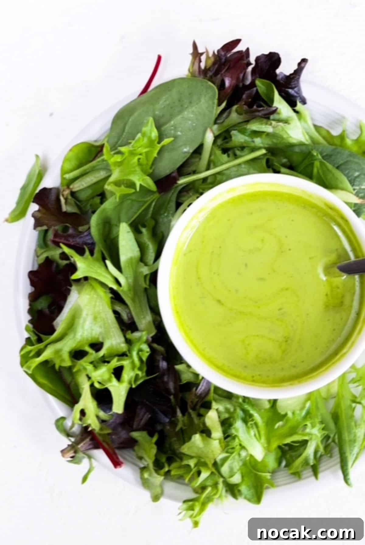 Basil Balsamic Vinaigrette Recipe — Fresh Homemade Dressing 2 A small bowl of Basil Balsamic Dressing with a simple lettuce salad on a white plate.