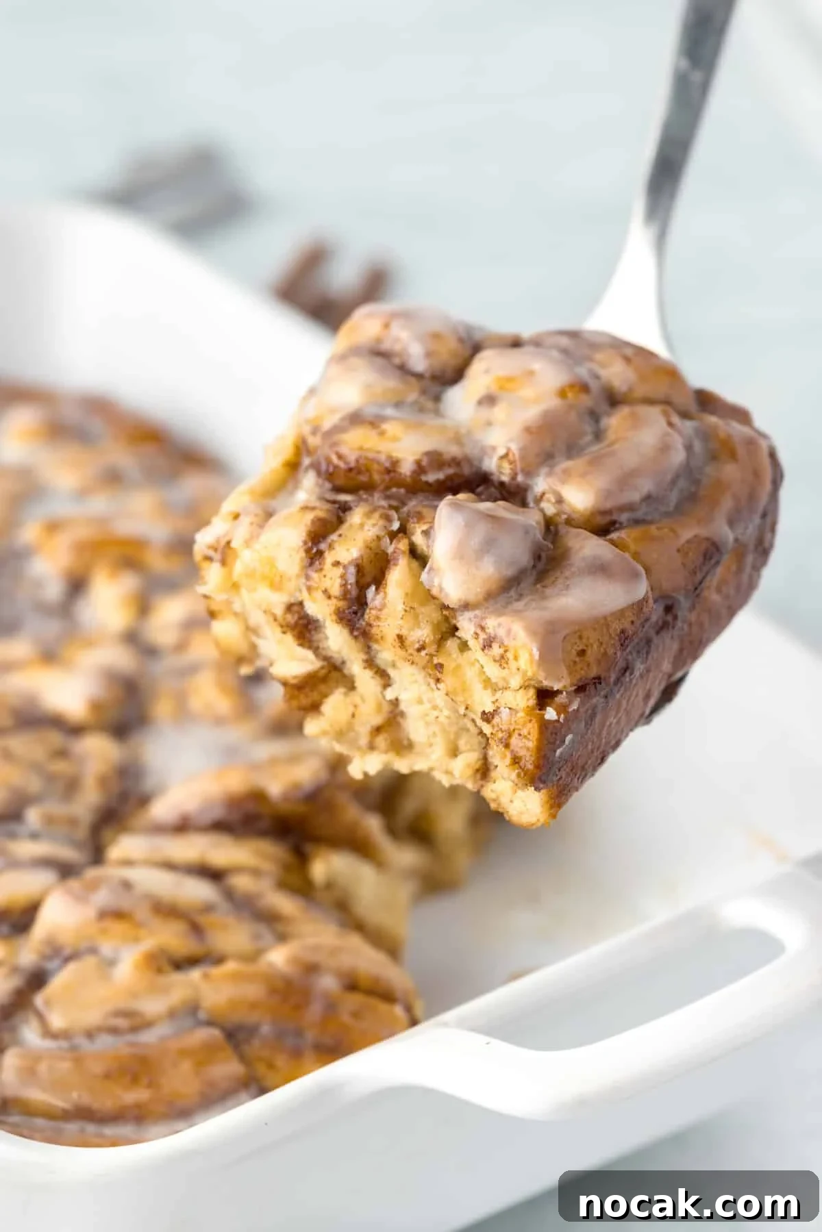 Cinnamon Roll Casserole Breakfast Bake Recipe 12 Lifting a portion of cinnamon roll breakfast bake from a baking dish.