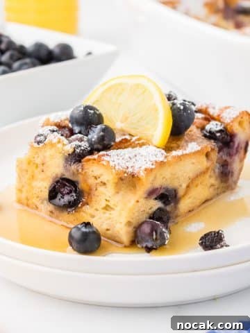 A square of baked French toast garnished with lemon and blueberries.