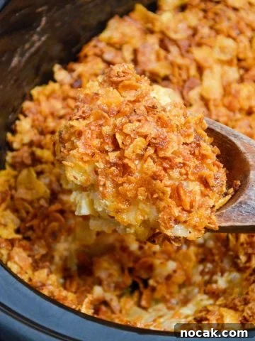 A large wooden spoon scoops up a portion of funeral potatoes made in a slow cooker.