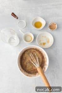 Cinnamon Roll Casserole Breakfast Bake Recipe 22 Whisking together ingredients in a bowl, with empty cups and bowls surrounding it.