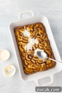 Cinnamon Roll Casserole Breakfast Bake Recipe 24 Spreading glaze on a baking dish with baked cinnamon roll pieces.