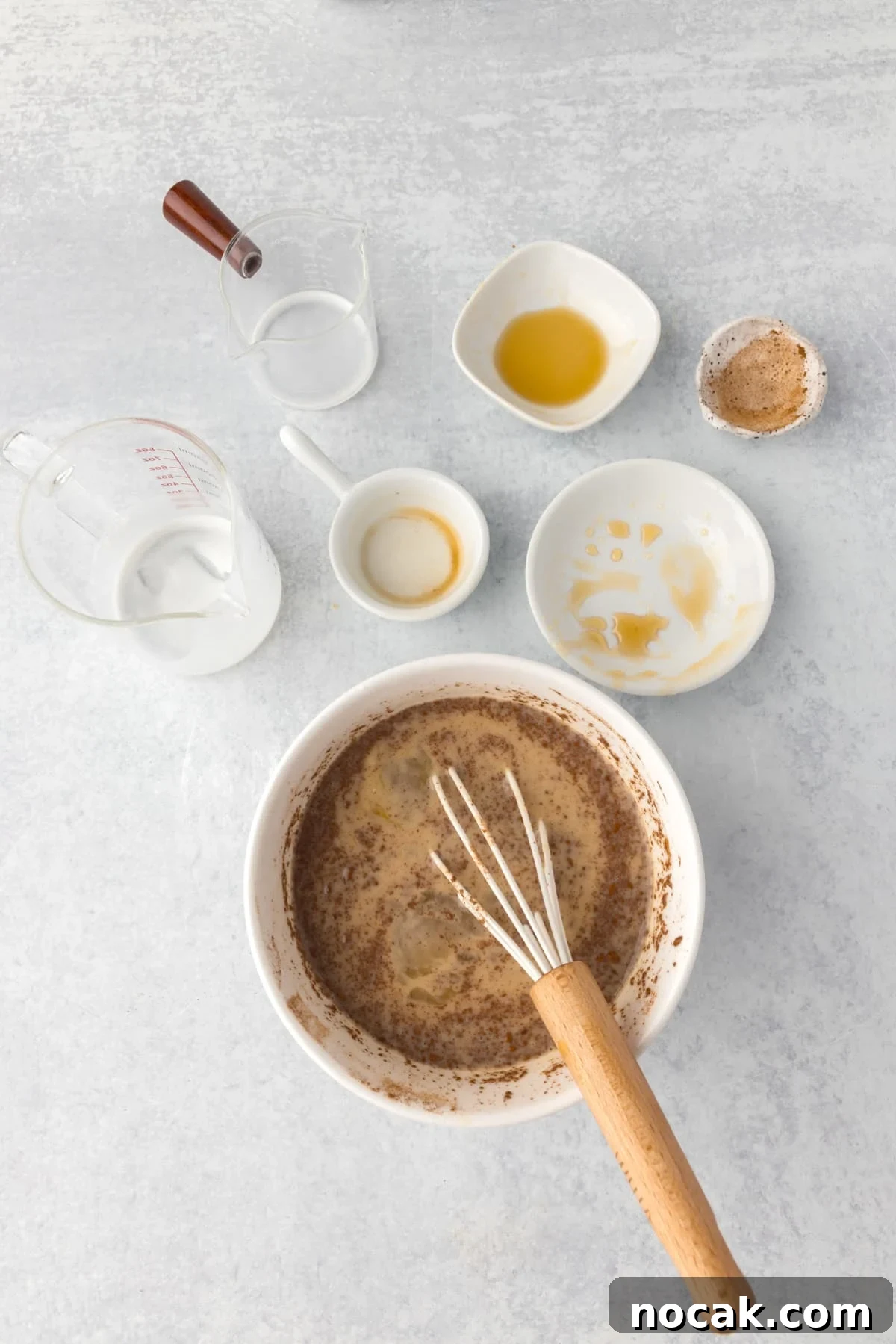 Cinnamon Roll Casserole Breakfast Bake Recipe 7 Whisking together ingredients in a bowl, with empty cups and bowls surrounding it.