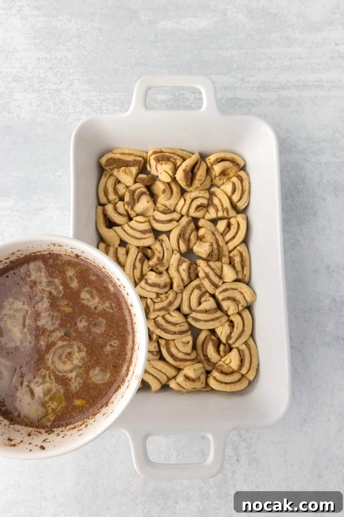 Cinnamon Roll Casserole Breakfast Bake Recipe 8 Pouring a custard mixture over a baking dish filled with cinnamon roll pieces.