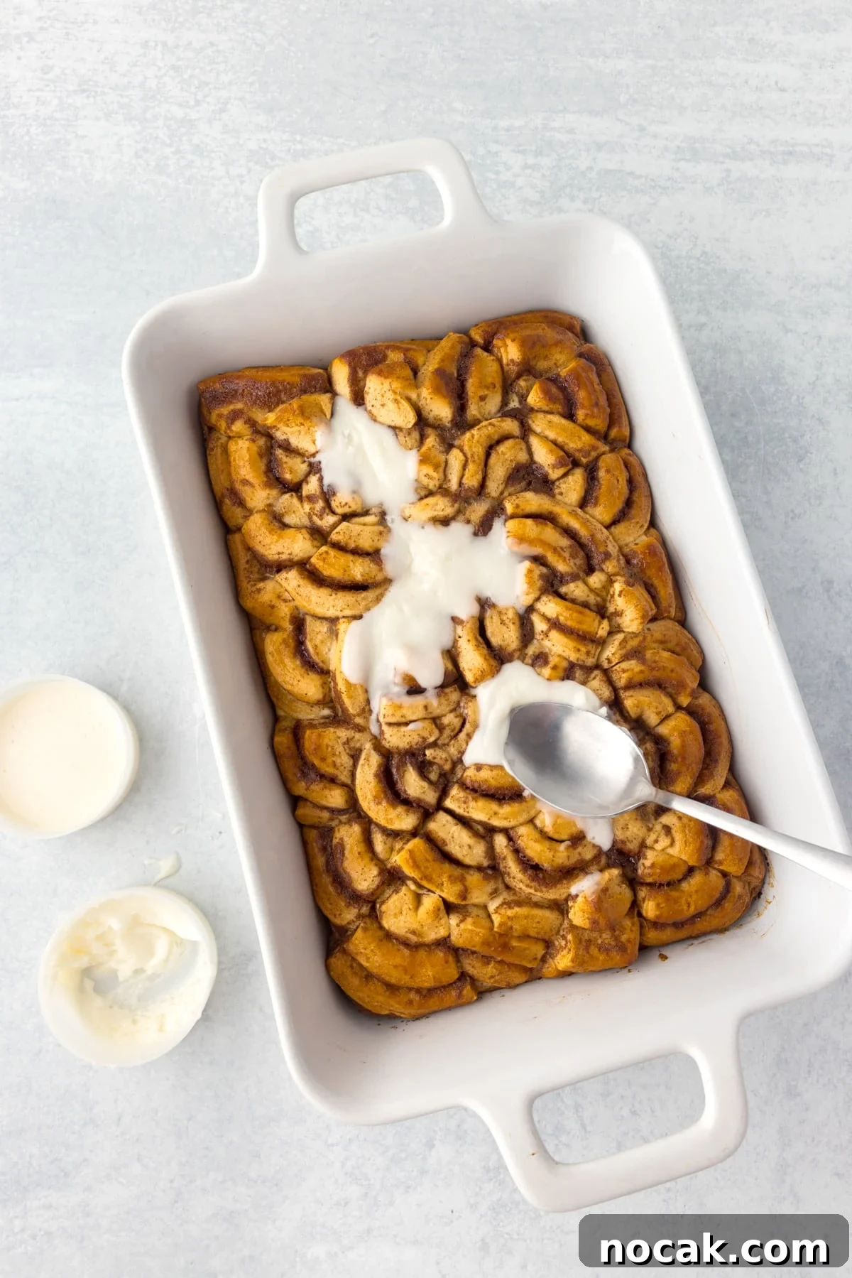 Cinnamon Roll Casserole Breakfast Bake Recipe 10 Spreading glaze on a baking dish with baked cinnamon roll pieces.