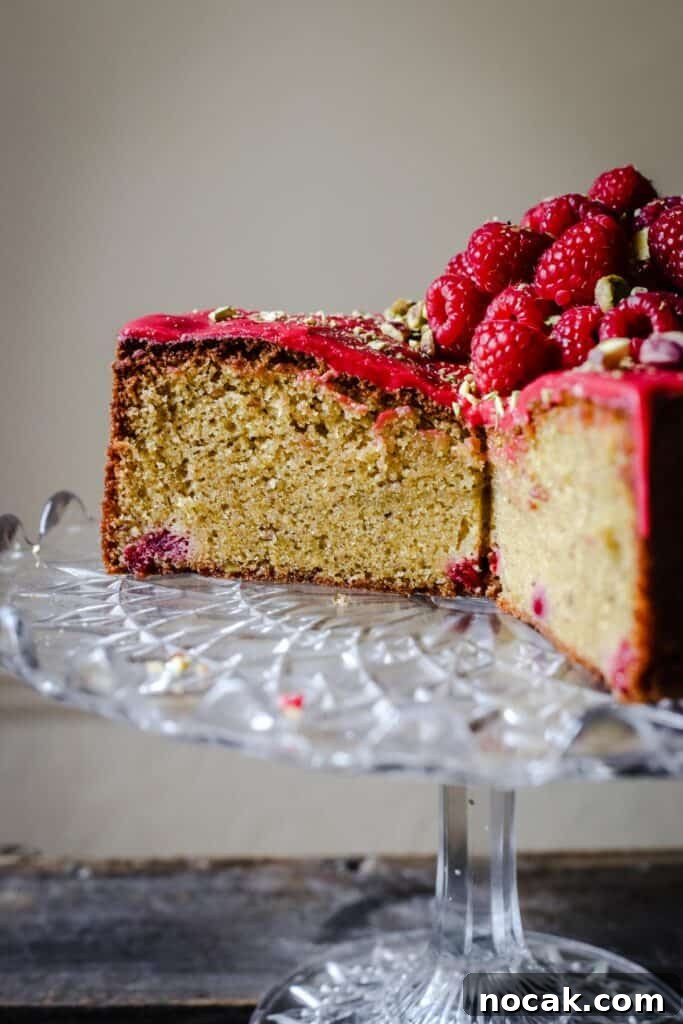 Gluten-Free Raspberry and Pistachio Cake Recipe 5 A cut Raspberry Pistachio Cake sitting on a cake stand on a wooden table