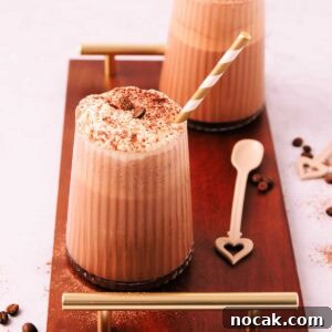 Creamy Mocha Milkshake Recipe: How to Make the Perfect Coffee Chocolate Shake 8 Two mocha milkshakes in glasses with a ribbed texture, topped with whipped cream and a sprinkle of cocoa, with gold and white striped paper straws on a dark wooden board with gold handles.