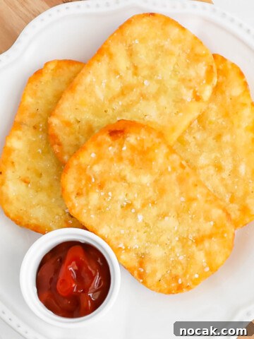 Four crispy hash browns on a plate with a small dish of ketchup.