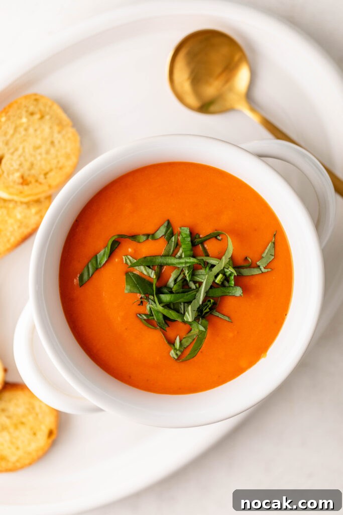 Creamy Sheet-Pan Roasted Tomato Soup 2 bowl of creamy roasted tomato soup topped with fresh basil on a plate with garlic crostini and a gold spoon